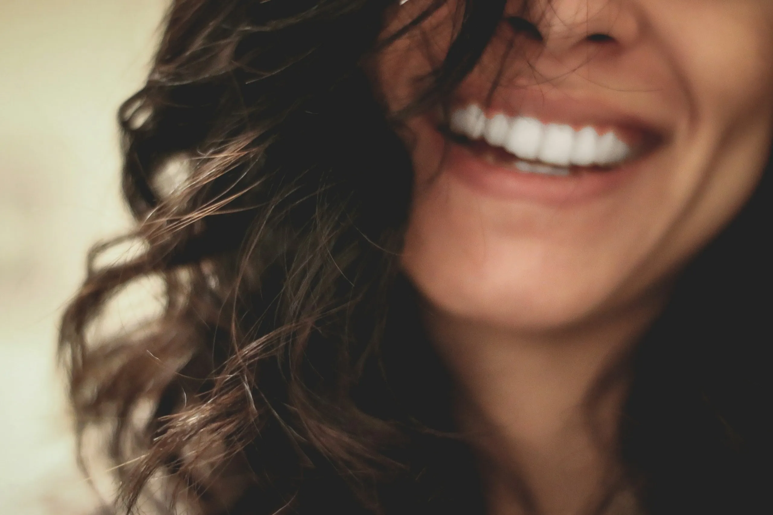Gros plan photographique d’un sourire naturel, entouré de cheveux bruns.
