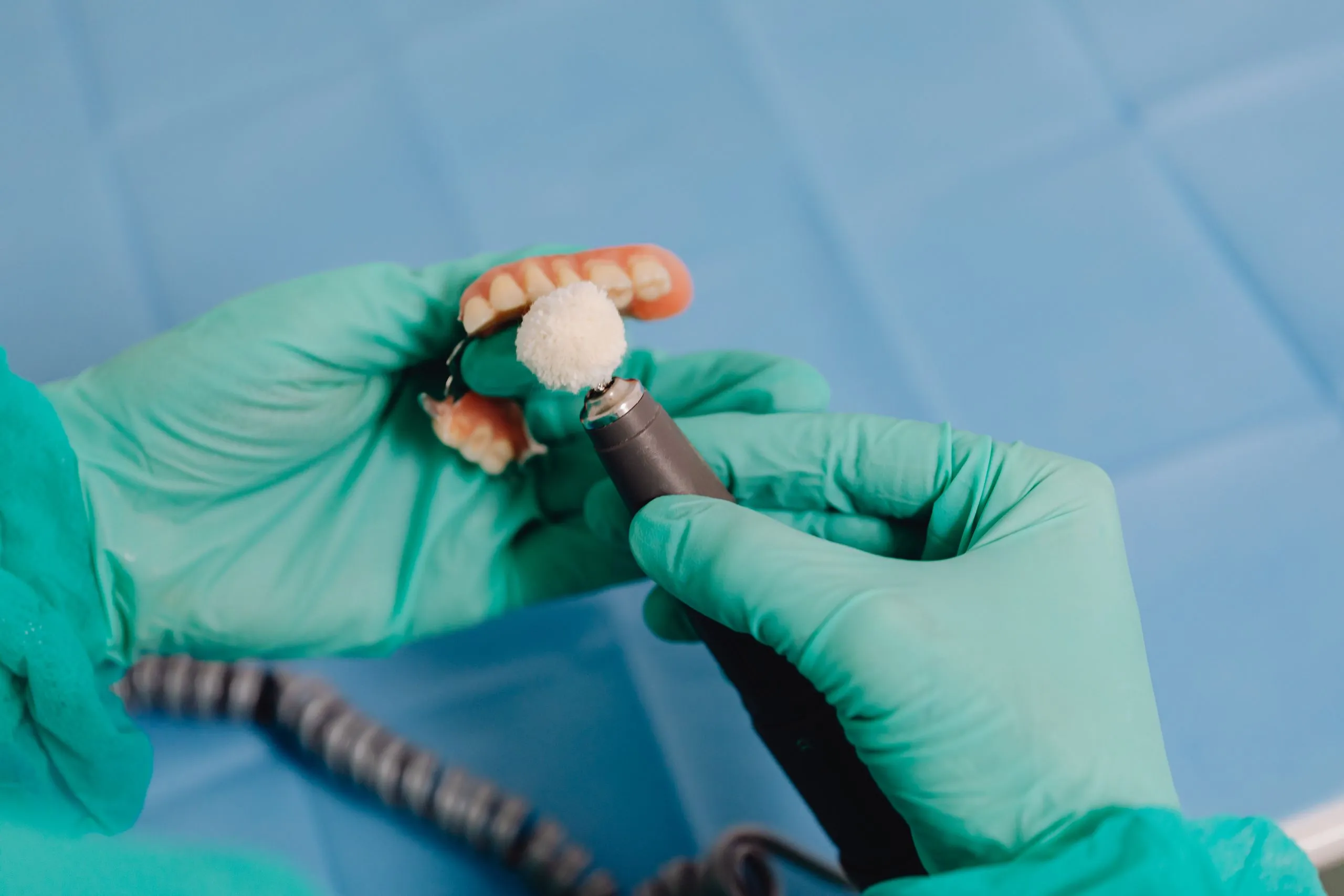 Deux mains gantées ajustent une prothèse dentaire à l’aide d’un instrument de précision.